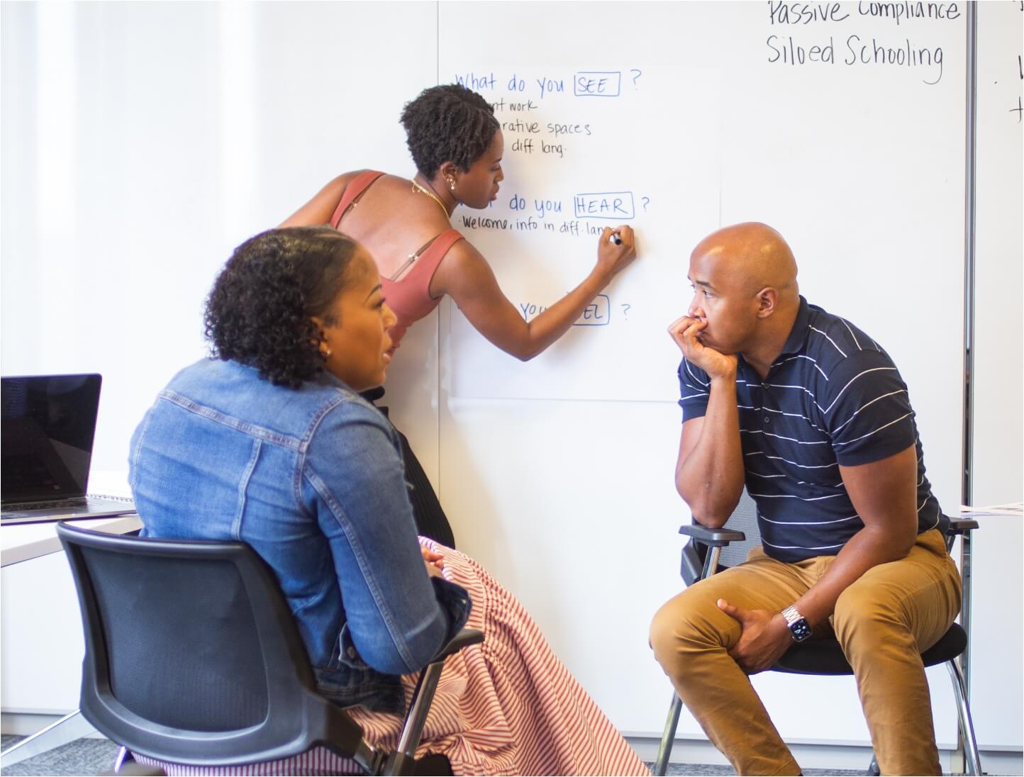 Three Springpoint fellows having a discussion in a room. One person writes on a whiteboard while two others sit and listen attentively.