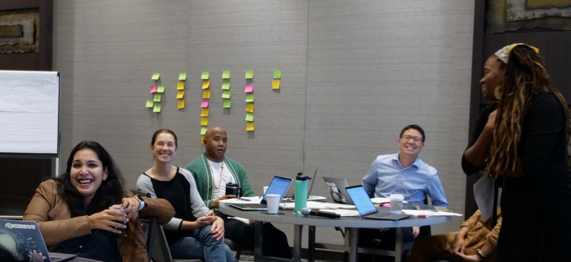 Springpoint Fellows sitting around a conference table with laptops and papers, smiling. Sticky notes are on the wall behind them.